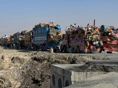 Afghan refugees sit beside trucks loaded with their belongings as they wait their turn to leave for their homeland through a border crossing point which partially opens following Oct.19 ceasefire, on the outskirts of Chaman, a border town on the Pakistan Afghan border, Wednesday, Oct. 29, 2025. (AP Photo/H. Achakzai)
