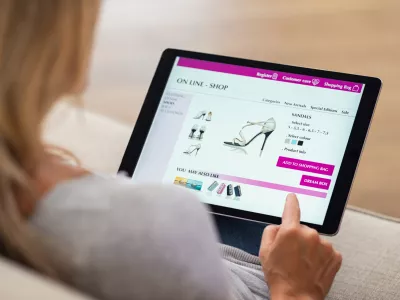 Closeup of woman doing online shopping on digital tablet at home. Rear view of woman hand touching screen while selecting shoes on ecommerce portal. Lady use e-commerce webshop to buy shoes.