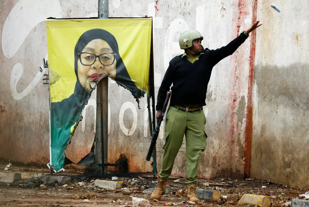 A Tanzanian riot police officer throws a used teargas canister near a vandalised campaign poster of President Samia Suluhu Hassan, following a protest a day after a general election marred by violent demonstrations over the exclusion of two leading opposition candidates at the Namanga One-Post Border crossing point between Kenya and Tanzania, October 30, 2025. REUTERS/Thomas Mukoya