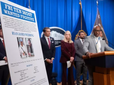 Akil Davis, assistant director in charge of the FBI's Los Angeles Field Office, looks at a wanted poster for Canadian fugitive Ryan James Wedding as he speaks with reporters during a news conference at the Department of Justice, Wednesday, Nov. 19, 2025, in Washington. (AP Photo/Mark Schiefelbein)