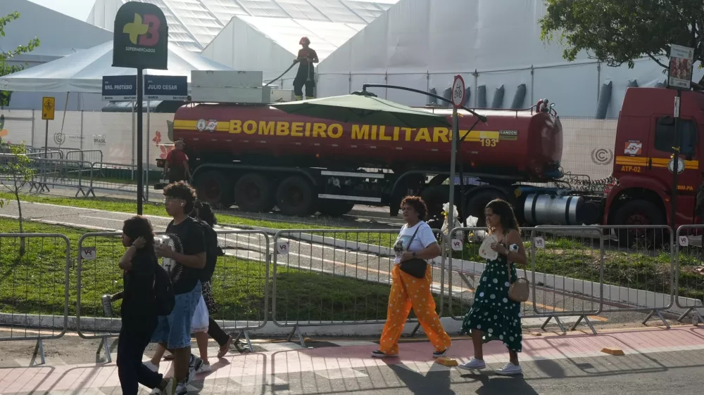 People walk past as a firefighter works at the COP30 U.N. Climate Summit following a fire, Thursday, Nov. 20, 2025, in Belem, Brazil. (AP Photo/Fernando Llano)