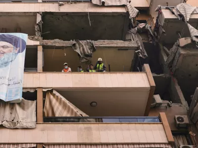 A large banner depicting Hezbollah's late leader Hassan Nasrallah hangs from a damaged balcony as civil defense workers clear the rubble in a residential building that was hit in Sunday's Israeli airstrike killing Hezbollah's chief of staff, Haytham Tabtabai in the southern suburb of Hareit Hreik, Beirut, Lebanon, Monday, Nov. 24, 2025. (AP Photo/Hassan Ammar)