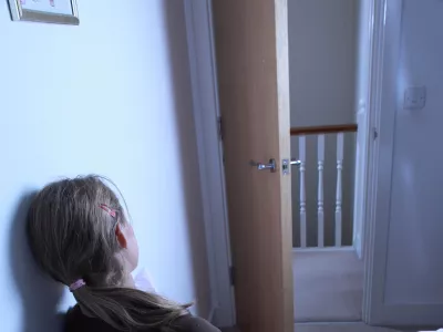teenage girl sitting alone on her bed, back to camera.