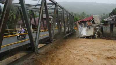 Motorists ride on a bridge past buildings damaged by flooding in Tanah Datar, West Sumatra, Indonesia, Friday, Nov. 28, 2025. (AP Photo/Ali Nayaka)