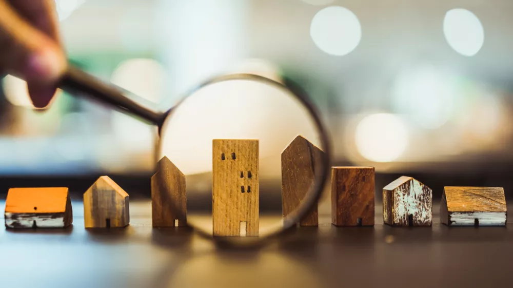 Hand holding magnifying glass and looking at house model, house selection, real estate concept.