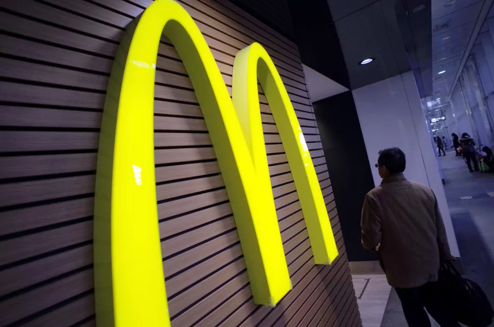 FILE - In this Dec. 17, 2014 file photo, a man walks by a McDonald's logo in front of its restaurant in Tokyo. McDonald's is set to unveil its latest plans to revive its sputtering business on Monday, May 4, 2015. (AP Photo/Eugene Hoshiko, File)