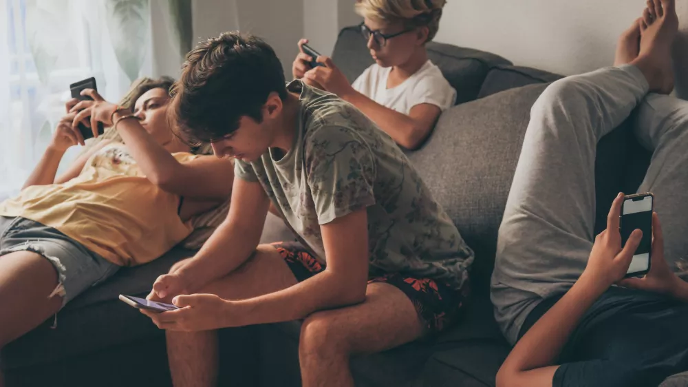 Group of teenager using smartphone sitting on a sofa at home. Young boys and a girl sharing photo and video watching social story online. Friends enjoying new trend technology. Youth and tech concept / Foto: Fabio Principe