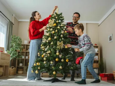 Happy family decorating beautiful christmas tree with golden and white ornaments and warm lights, enjoying their time together during winter holidays