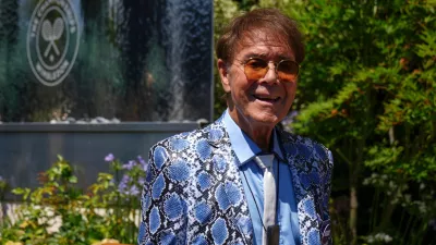 FILE - Singer Cliff Richard poses for a photo as he arrives for day eleven at the Wimbledon Tennis Championships in London, July 10, 2025. (AP Photo/Joanna Chan, File)
