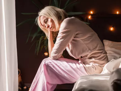 Upset middle-aged woman sit on bed in bedroom lost in thoughts thinking pondering of problem solution, depressed unhappy mature female look in distance suffer from depression, having personal problems