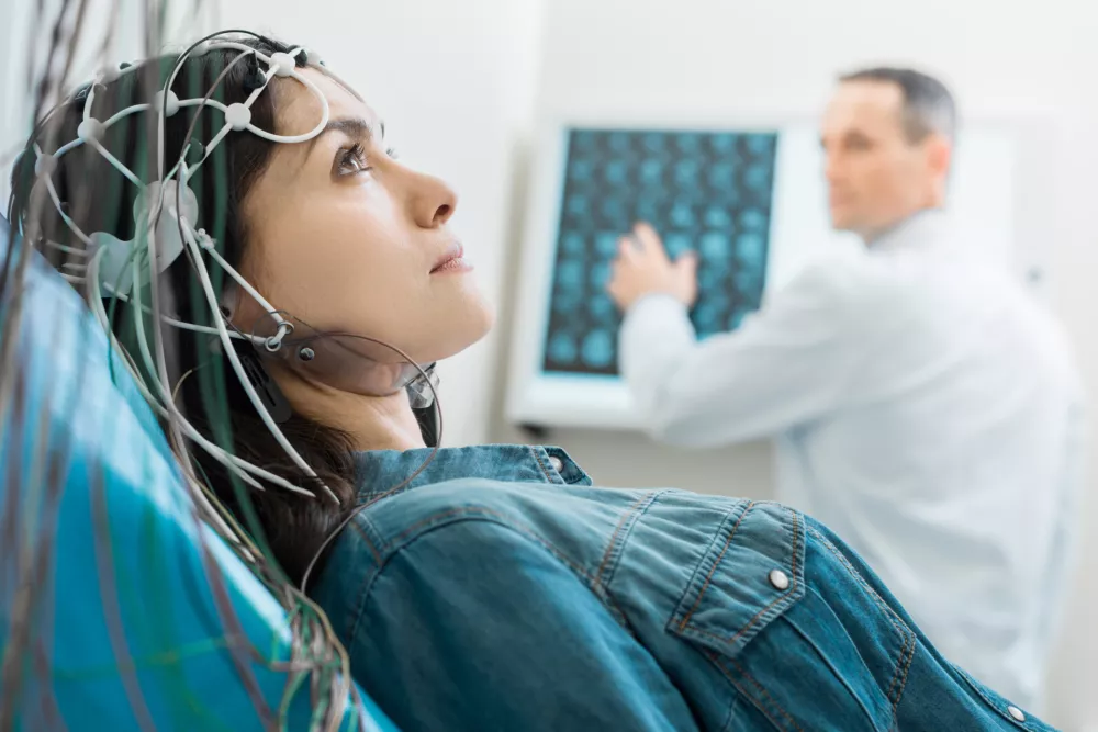 Vital procedure. Beautiful dark-haired woman lying on an examination table and undergoing electroencephalography while her doctor examining CT results / Foto: Yacobchuk