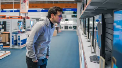 Smart modern male customer examining large TV-sets at electronics store. He looks at new display.. New screen generations.
