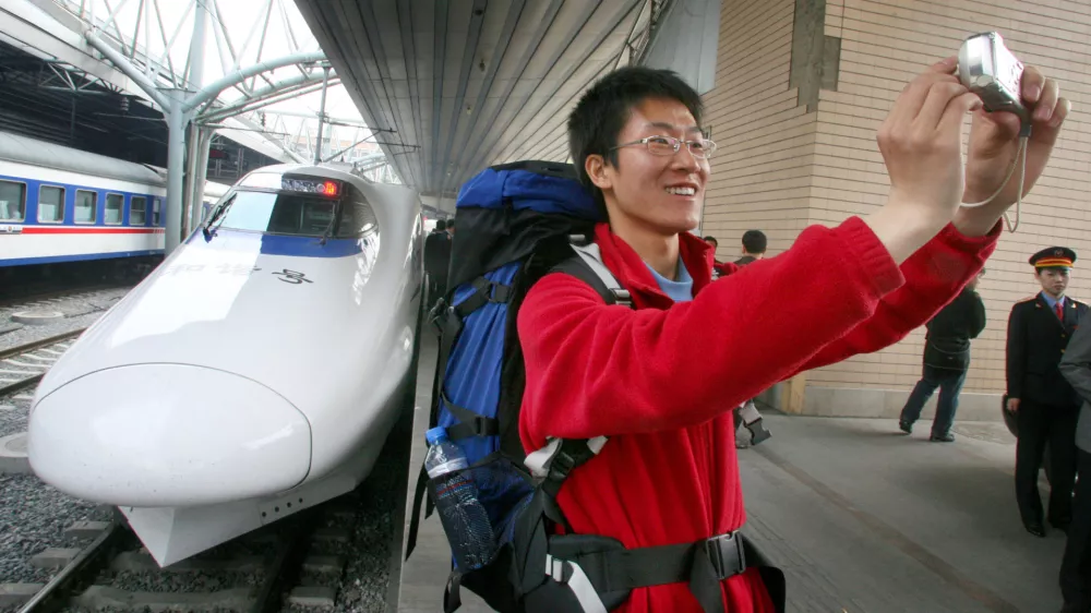 A traveler takes a snapshot of him with a bullet train in the backdrop at the train station in Beijing Wednesday, April 18, 2007. Faster Chinese trains running at about 200 kph (124 mph) began service Wednesday as part of a bid to keep up with ballooning transport demand, state media reported. (AP Photo/EyePress) ** CHINA OUT **