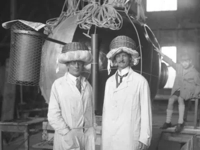 Prof. Piccard wieder fertig zu seinem grossen Stratosph?ren-Flug!Der Br?sseler Prof. August Piccard (rechts) und sein Begleiter, der Schweizer Ing. Kipfer (links) mit ihrem aus N?hk?rben verfertigten Sturzhelmen vor der Kugel, fertig zum Stratosph?renflug in 16.000 m H?he. / Foto: O.ang.