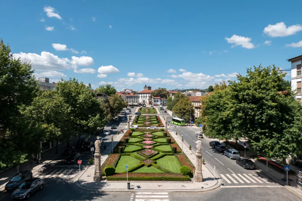 Panoramic view of the garden of Alameda da Rep&uacute;blica in Guimar&atilde;es, featuring formally trimmed boxwood hedges and flower beds, flanked by statues and traditional buildings in Portugal