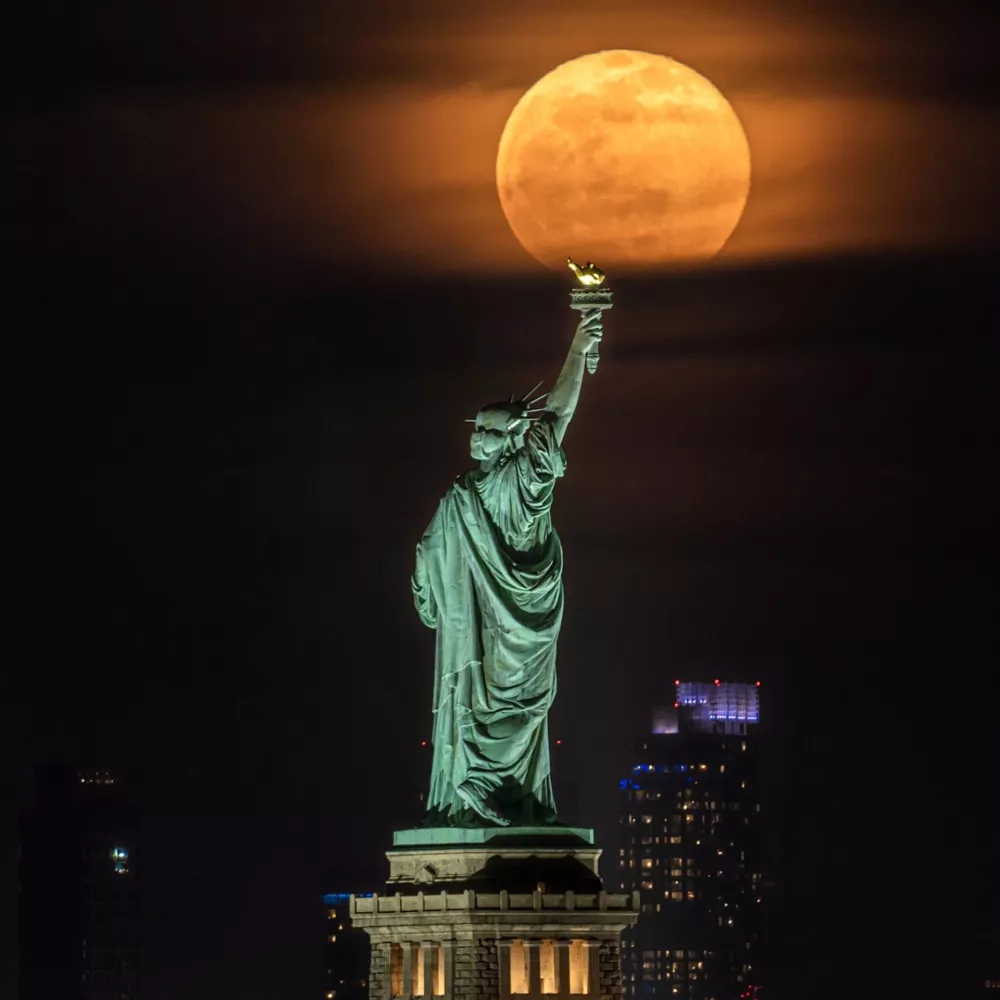 A majestic full moon rises behind the Statue of Liberty in New York Harbor, casting a soft glow on one of America's most iconic monuments. Captured during a clear night, this image blends celestial beauty with the enduring symbol of freedom and hope. / Foto: Aniket Dharmik