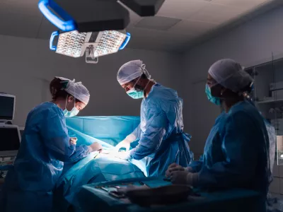 An intricate surgical procedure in progress with healthcare professionals in full surgical gear, under bright operating room lights, emphasizing the modern medical equipment and organization.