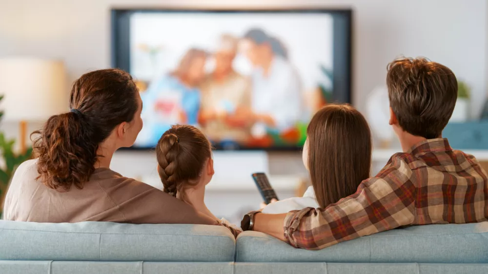 Happy family spending time together. Mother, father and children watching TV, movies with popcorn in the evening at home.