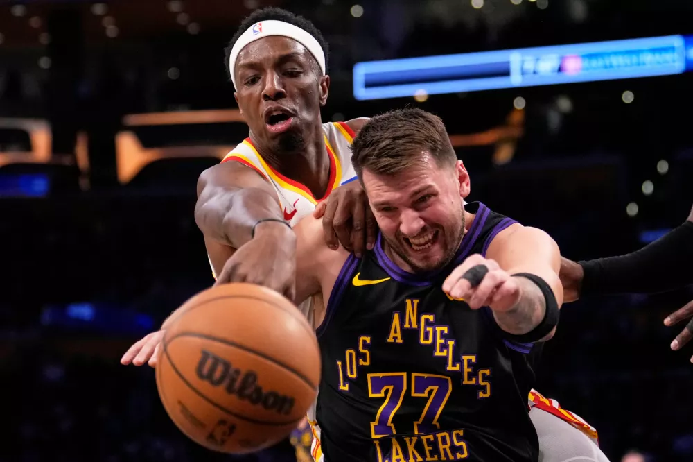 Atlanta Hawks forward Onyeka Okongwu, left, and Los Angeles Lakers guard Luka Doncic reach for a loose ball during the first half of an NBA basketball game Tuesday, Jan. 13, 2026, in Los Angeles. (AP Photo/Mark J. Terrill)