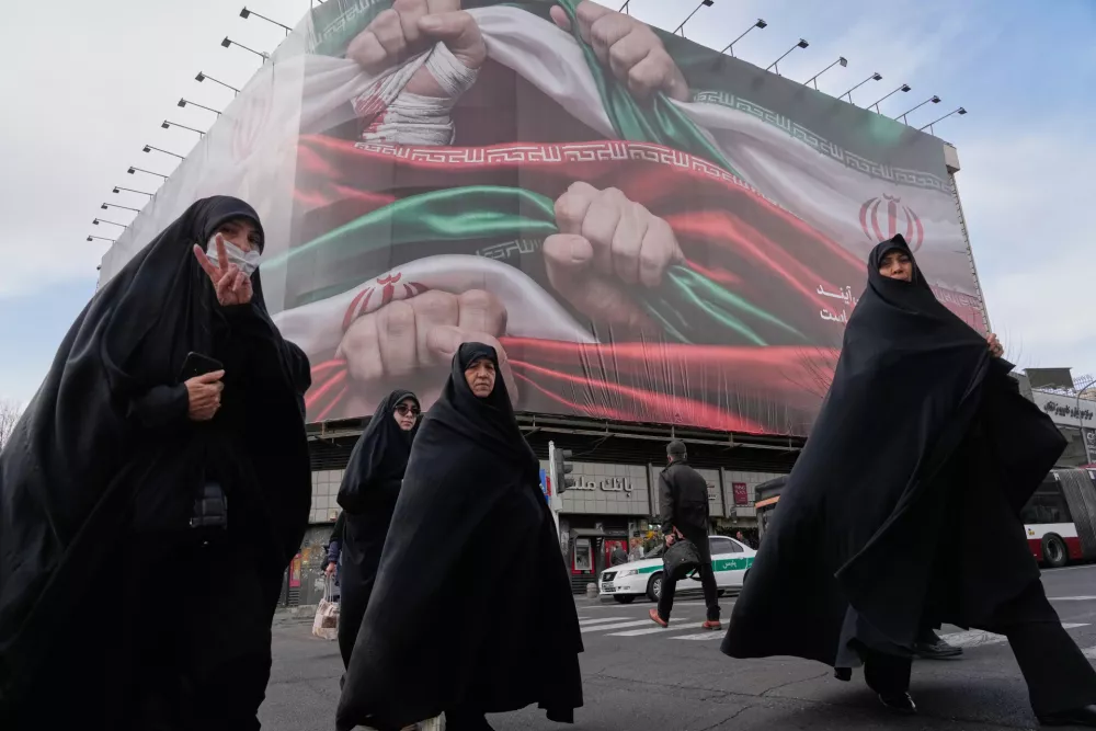 FILE - Women cross a street under a huge banner showing hands firmly holding Iranian flags as a sign of patriotism in Tehran, Iran, Jan. 14, 2026. (AP Photo/Vahid Salemi, File)