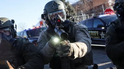 A Law enforcement member holds a weapon as they stand guard while people protest outside the Bishop Henry Whipple Federal Building, after the fatal shootings of Renee Nicole Good and Alex Pretti by federal immigration agents, in Minneapolis, Minnesota, U.S., January 30, 2026. REUTERS/Shannon Stapleton   TPX IMAGES OF THE DAY