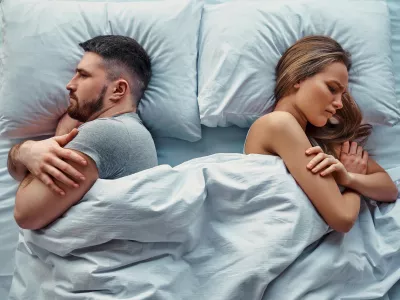 Young beautiful couple lying in bed turned back to back, arms crossed in anger and resentment. Relationship problems.Top view. / Foto: Harbucks
