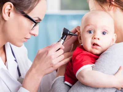 Young doctor examining baby boy with otoscope