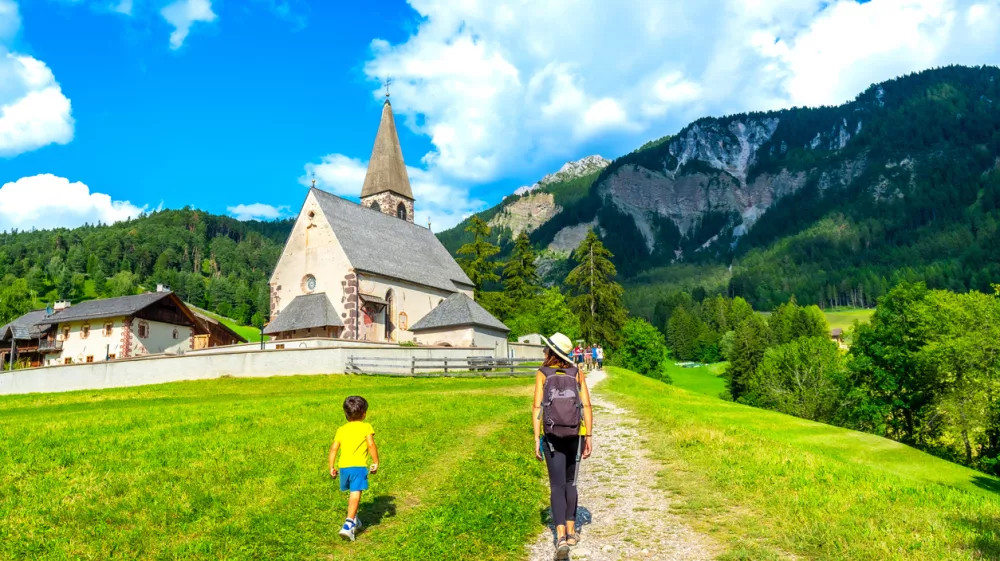 Tourists walking on a path towards the church of st. Magdalena in the italian dolomites on a beautiful summer day