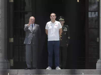 Photographed through a gate, Peru's President Jose Jeri, right, stands with Prime Minister Ernesto Alvarez during the changing of the guard ceremony at the government palace in Lima, Peru, Tuesday, Feb. 17, 2026. (AP Photo/Gerardo Marin)
