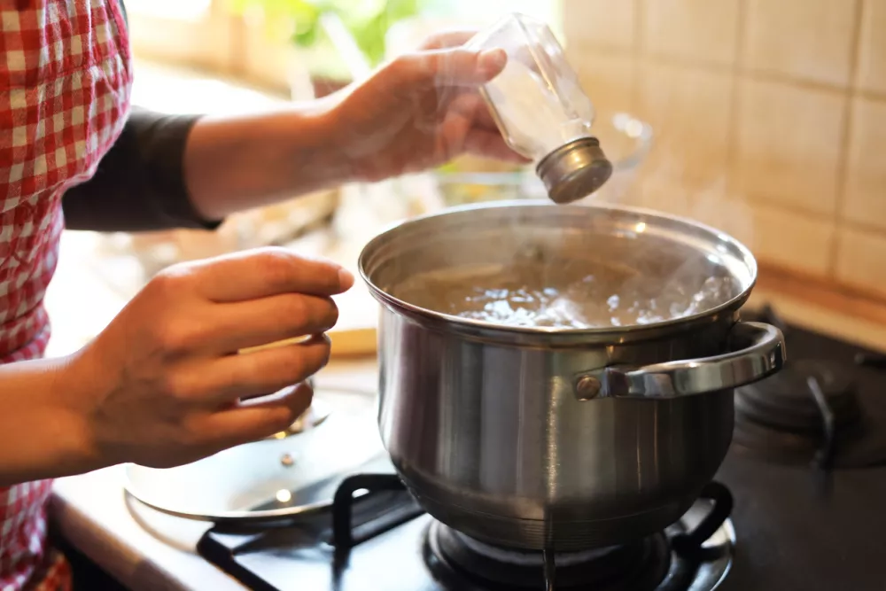 Woman adding salt to boiling water in pot on stove indoors, closeup / Foto: Liudmila Chernetska