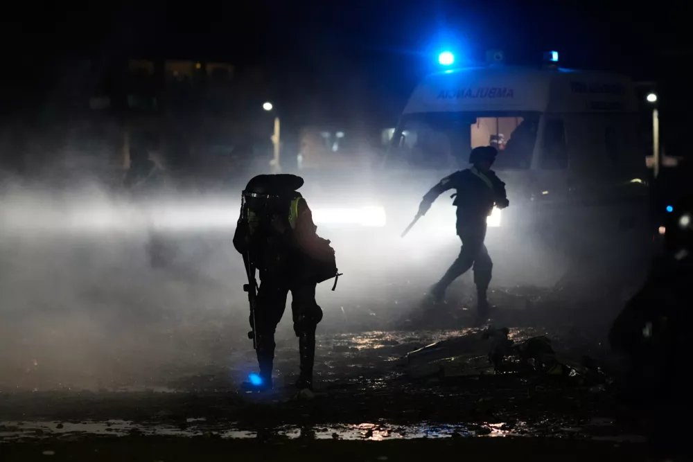 A police covers himself from tear gas spread to disperse people from getting near the area where a aircraft that was transporting money crashed on a highway, in El Alto, Bolivia, Friday, Feb. 27, 2026. (AP Photo/Juan Karita)