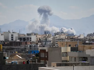 People watches from rooftop as a plume of smoke rises after a strike in Tehran, Iran, Sunday, March 1, 2026. (AP Photo/Vahid Salemi)