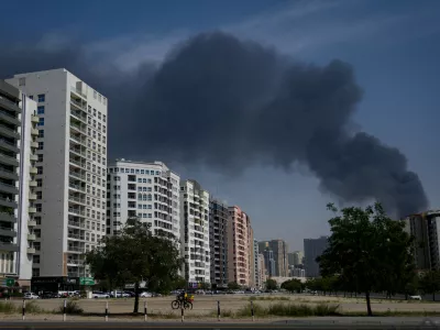 A cyclist rides past as black plume of smoke is seen rising from a warehouse at the industrial area of Sharjah City in the United Arab Emirates following reports of Iranian strikes in Dubai, United Arab Emirates, Sunday, March 1, 2026. (AP Photo/Altaf Qadri)