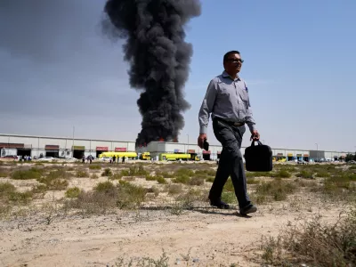 A man walks away after watching as a black plume of smoke rises from a warehouse in the industrial area of Sharjah City, United Arab Emirates, Sunday, March 1, 2026, following reports of Iranian strikes in Dubai. (AP Photo/Altaf Qadri)