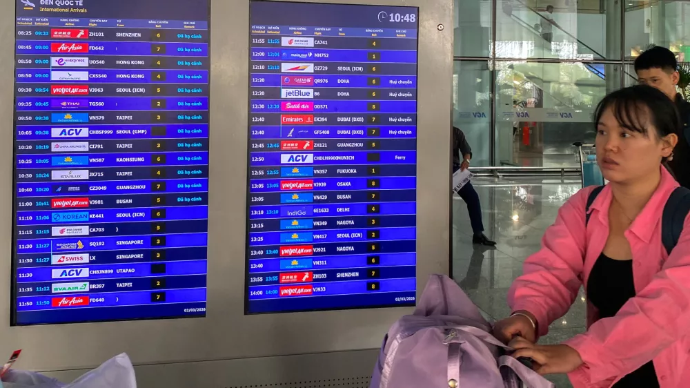 Passengers walk past a display board showing canceled flights to Dubai and Doha amid regional airspace closures at Noi Bai International Airport in Hanoi, Vietnam, March 2, 2026. Picture taken with a mobile phone. REUTERS/Thinh Nguyen