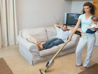 ženska čisti, či&scaron;čenje, pospravljanje, gospodinjska dela Full length portrait of woman cleaning house while carrying baby with man relaxing on sofa,Image: 184546642, License: Royalty-free, Restrictions:, Model Release: yes