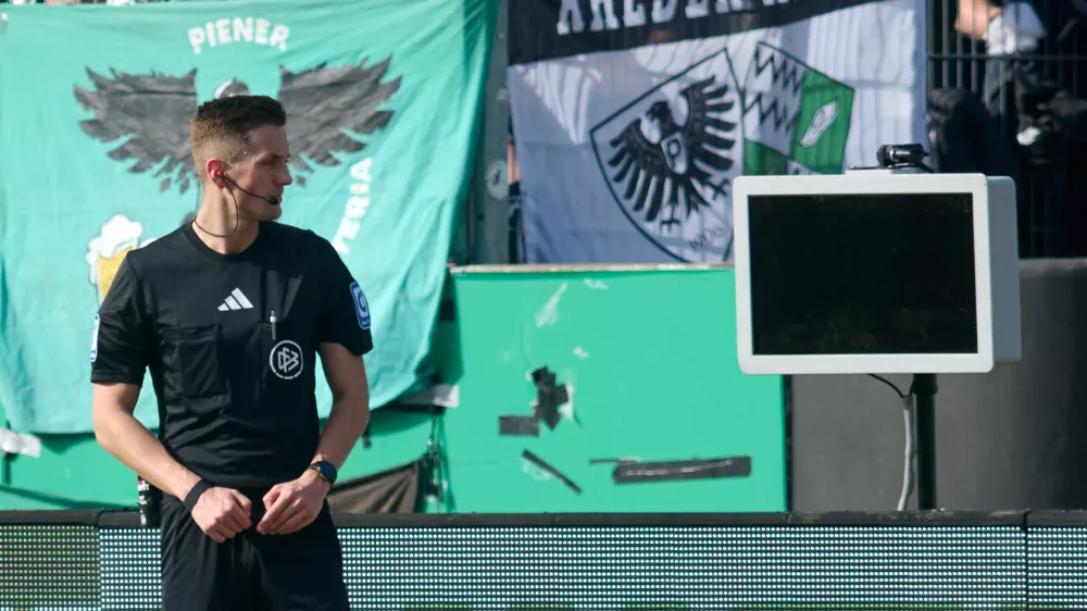 Referee Felix Bickel stands in front of the dark screen as he tries to review a VAR decision on a penalty kick for Berlin during the Bundesliga 2 soccer game between Muenster and Hertha Berlin in Muenster, Germany, Sunday March 8, 2026. (Bernd Thissen/dpa via AP)