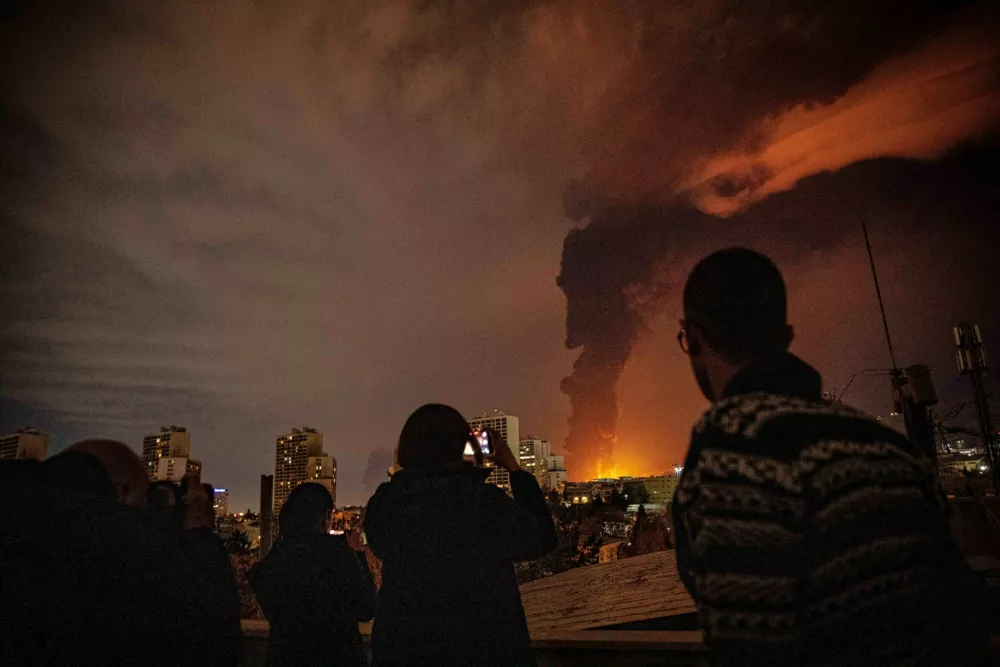Residents look on and take pictures as flames and smoke rise from an oil storage facility struck as attacks hit the city during the U.S.&ndash;Israeli military campaign in Tehran, Iran, Saturday, March 7, 2026. (Arileza Sotakbar/ISNA via AP)