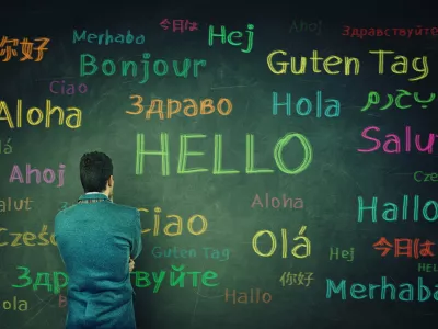 Rear view of a puzzled businessman in front of a huge chalkboard written with the word hallo in different languages and colors. Opportunity for learning many languages for students.