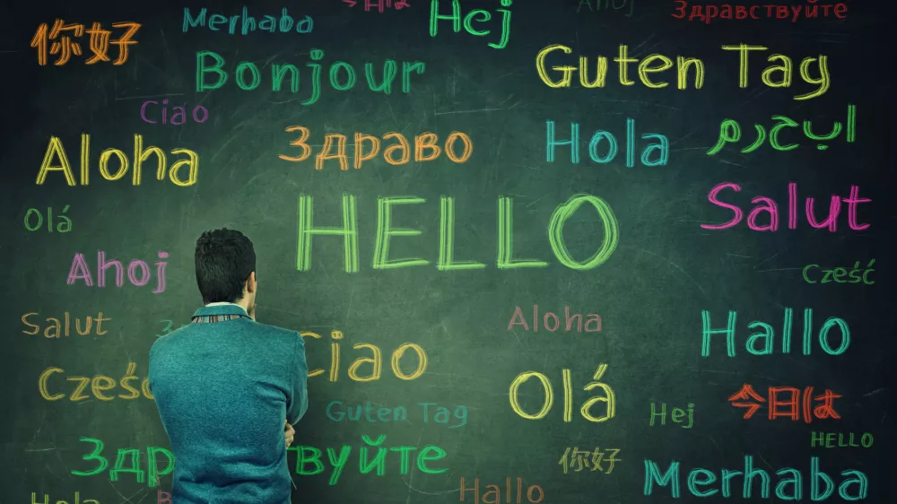 Rear view of a puzzled businessman in front of a huge chalkboard written with the word hallo in different languages and colors. Opportunity for learning many languages for students.