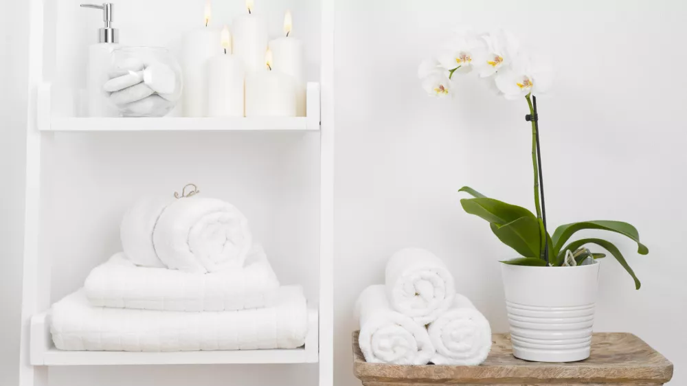 Shelf with clean towels, candles, flowerpot on bathroom wooden table