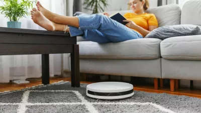 Robotic vacuum cleaner cleaning a room while a woman relaxing, reading book on the sofa. Innovative technologies for cleaning
