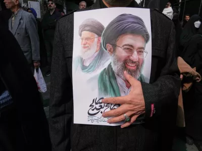 A mourner holds a poster depicting Ayatollah Mojtaba Khamenei, right, the successor to his late father Ayatollah Ali Khamenei, left, as supreme leader, during the funeral procession for senior Iranian military officials and civilians killed during the U.S.-Israel campaign in Tehran, Iran, Wednesday, March 11, 2026. (AP Photo/Vahid Salemi)