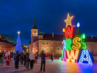 Warsaw, Poland - December 20, 2024: Illuminated Warszawa (Warsaw) sign and group of people on the Castle Square in the Old Town at night, Christmas time holiday season illumination.