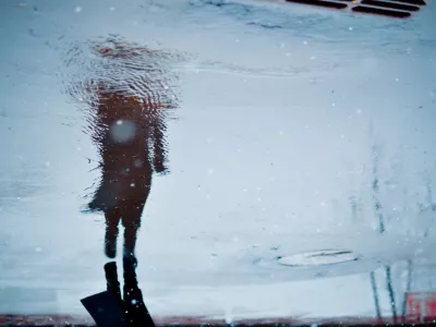 Depressed and loneliness mood concept. Blurry reflection in a rain puddle of alone walking person on wet city street during rainy weather.