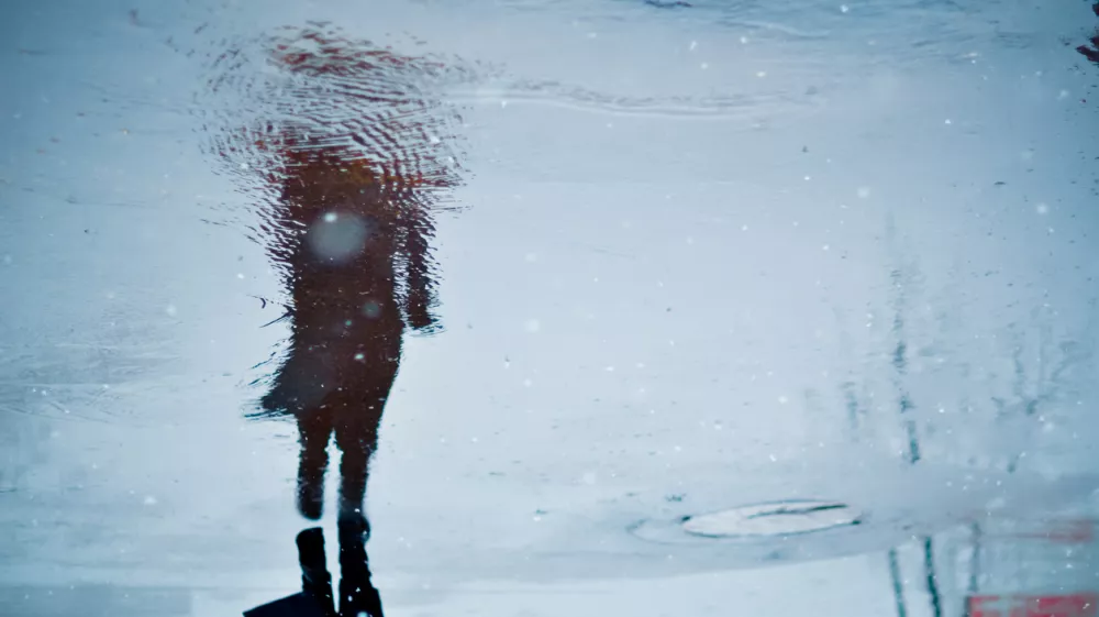 Depressed and loneliness mood concept. Blurry reflection in a rain puddle of alone walking person on wet city street during rainy weather.