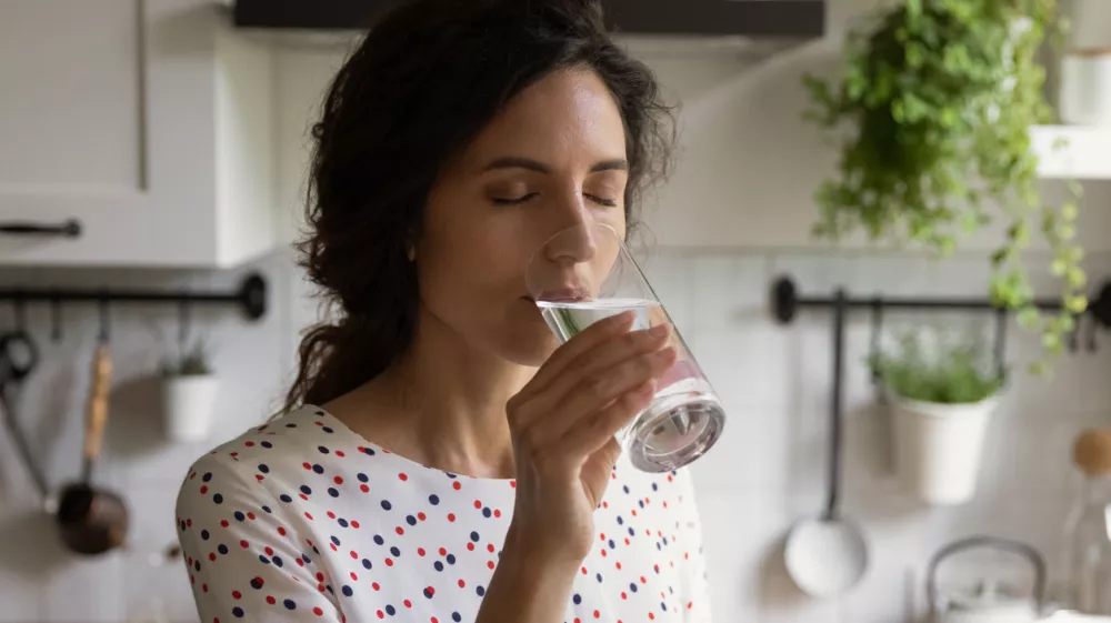 Pure pleasure. Thirsty millennial female drink swallow cool clear mineral aqua from glass at home kitchen feel delight. Young woman enjoy crystal filtered potable water with closed eyes relieve stress / Foto: Fizkes Getty Images