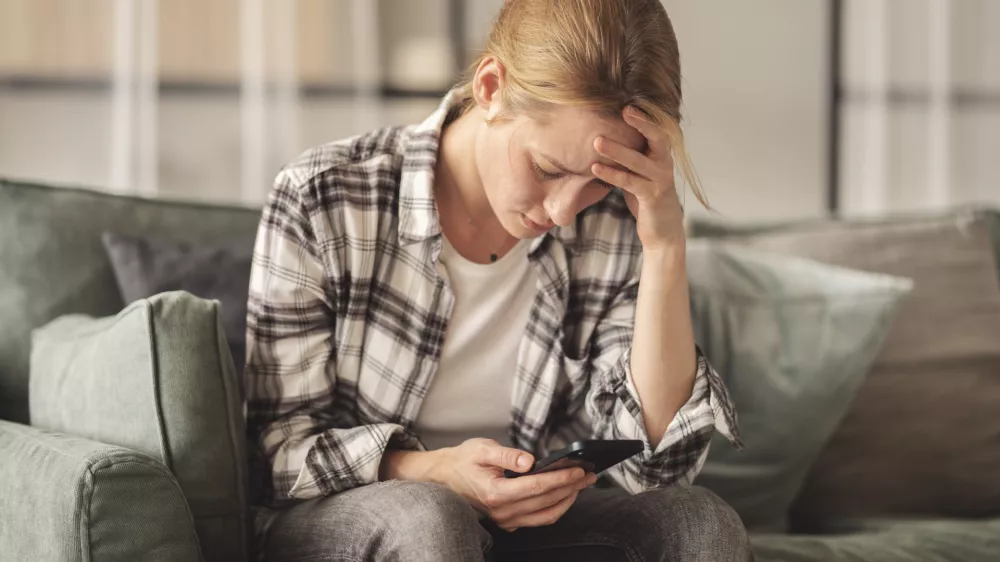 Woman reading some bad news on her smart phone, feeling sad and worried