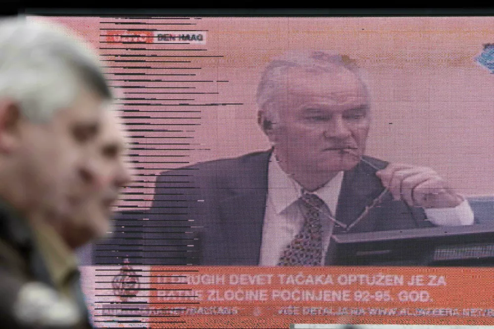 Bosnian people walking in a street pass a television screen in Sarajevo, Bosnia, on Wednesday, May 16, 2012 during a live TV broadcast as charges are read in court against Bosnian Serb Gen. Ratko Mladic at the U.N.'s Yugoslav war crimes tribunal in The Hague, Netherlands. Twenty years after Serb forces unleashed a brutal campaign of ethnic cleansing in Bosnia, their military commander Gen. Ratko Mladic is on trial Wednesday May 16, 2012, on charges of masterminding atrocities throughout the country devastating 1992-95 war.(AP photo/Amel Emric)