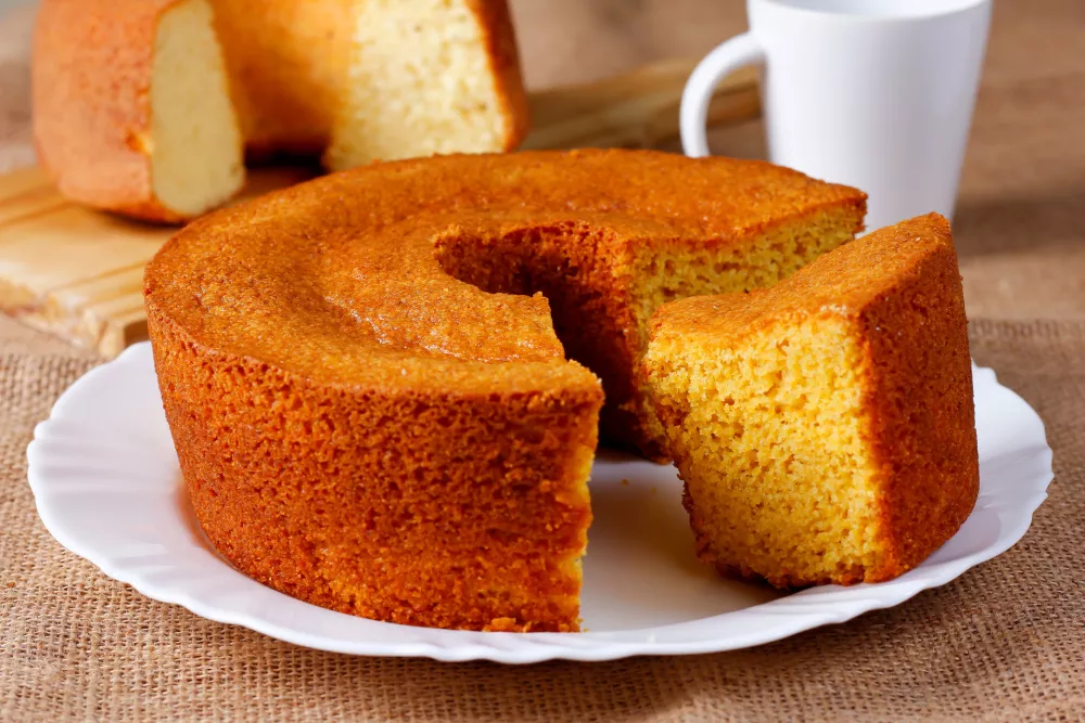 Homemade corn cake on white plate on rustic wooden table. Typical Brazilian party food. Selective focus / Foto: Gilnature